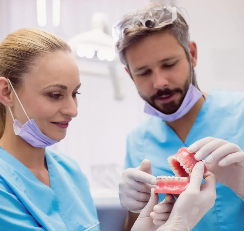 Dental consultation between a woman in scrubs and a man, discussing on a smartphone in a modern office setting.